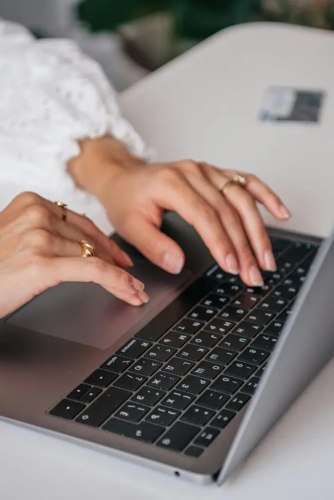 Hands of a woman typing on a laptop keyboard indoors, showcasing rings and fashion.